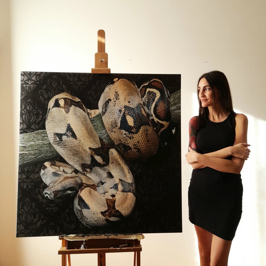 Claudia Daminato in the painting studio near the hyper-realistic painting of a python coiled around a trunk