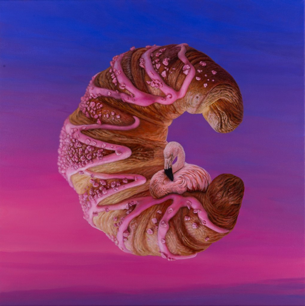 A C-shaped croissant with pink icing and a small flamingo against a sunset gradient.